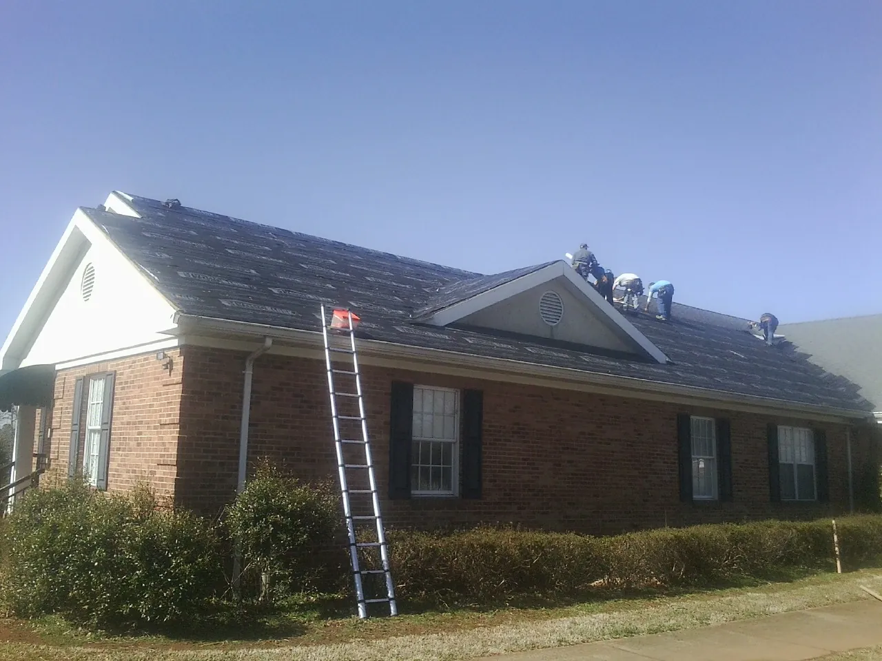 Crew tearing shingles off a brick ranch roof with a ladder set — Metal Roof Repair work by our crew in Decatur